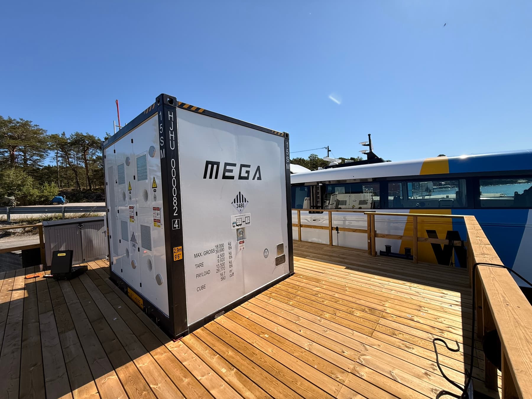MEGA:s mobila batterisystem på en brygga med en passagerarbåt i bakgrunden
